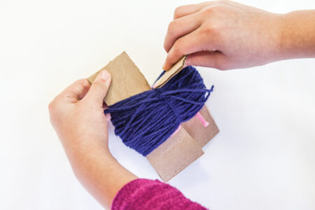 person tearing cardboard wrapped in blue yarn